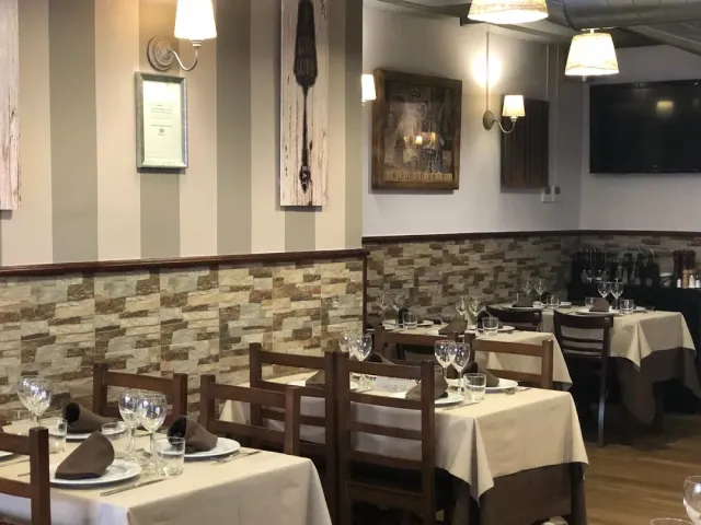 שולחנות ערוכים במפות בהירות מול קיר אבן מחופה ותמונות ממוסגרות