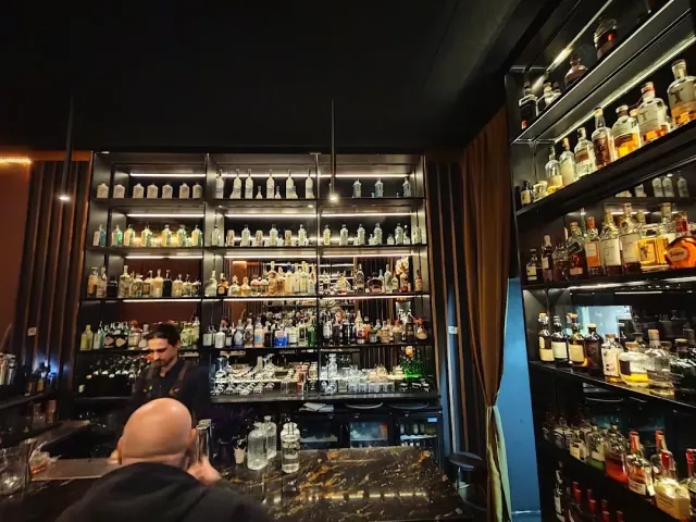 בר אפלולי עם מדפי בקבוקים מוארים עד התקרה וברמן מאחורי הדלפק