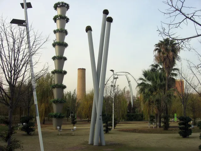 עמודי מתכת גבוהים עטופי צמחייה מטפסת מעל מדשאות ודקלים