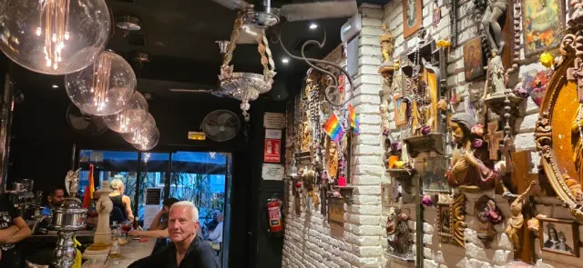 בר עם קיר לבנים עמוס פסלונים ומסגרות, נברשות זכוכית ודגל צבעוני