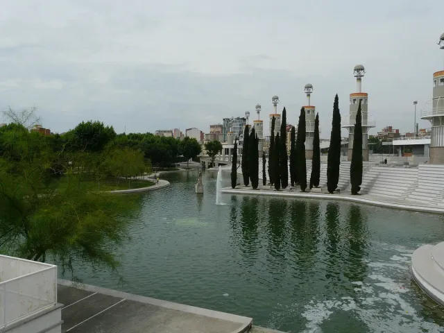 אגם ירוק בפארק עירוני עם שורת ברושים ומגדלי תצפית לבנים