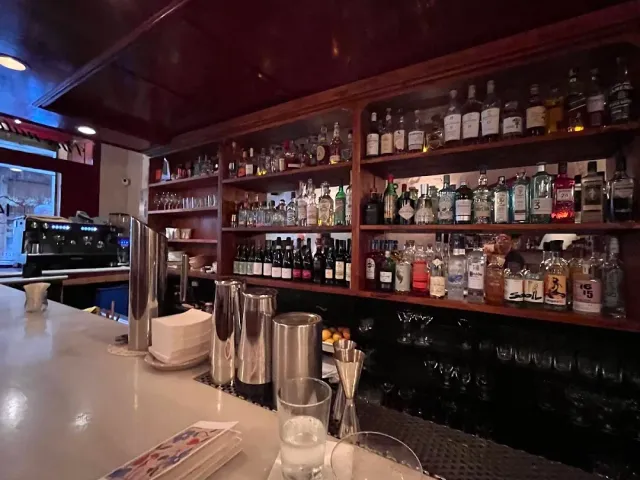 מדפי עץ עמוסים בבקבוקי אלכוהול מאחורי דלפק בהיר עם שייקרים מתכת