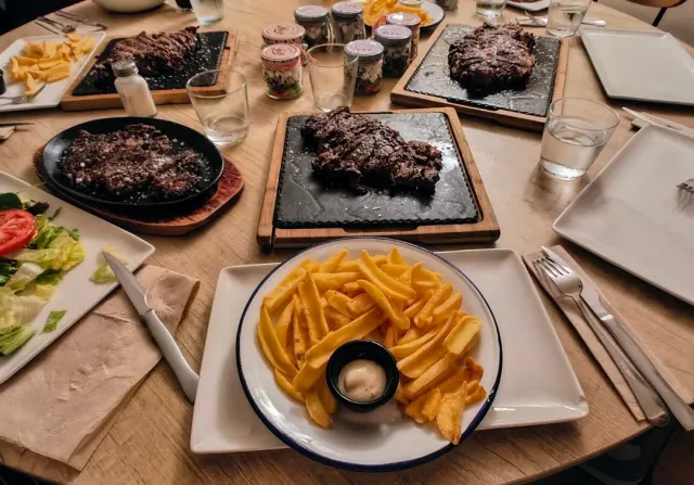 שולחן עמוס נתחי בשר על לוחות אבן, צלחת צ׳יפס וסלט ירקות
