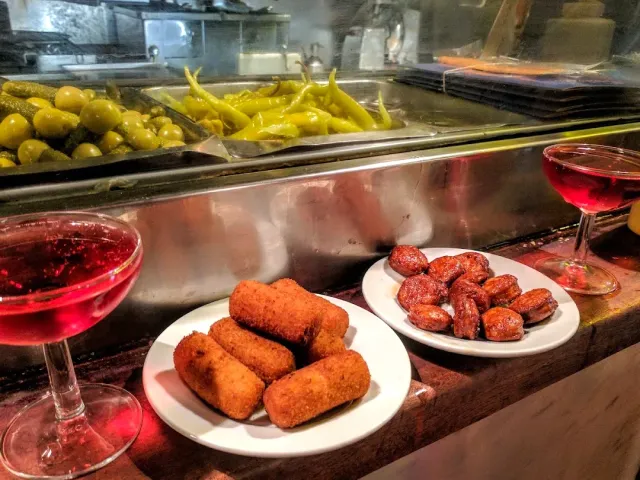 צלחת גלילי בצק מטוגנים וצלחת נקניקיות אדומות, לצד שתי כוסות משקה אדום