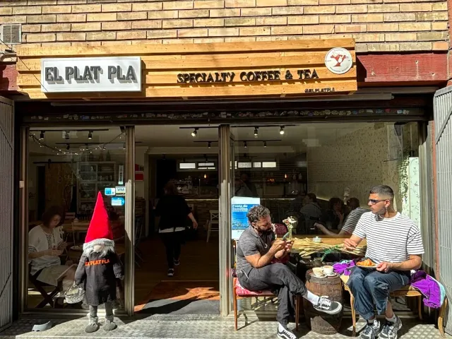 חזית פתוחה עם שלט עץ, יושבים על ספסלים בחוץ ופסל גמד בכניסה