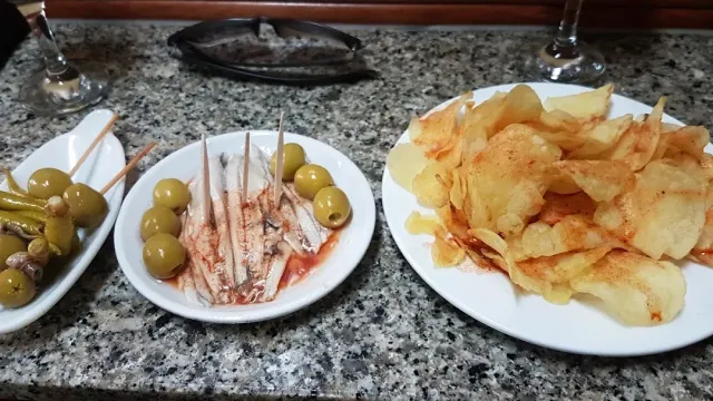 שלוש צלחות על שיש: פילה דגים עם זיתים, חמוצים על קיסם ופרוסות מטוגנות