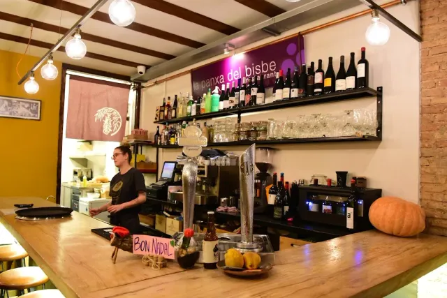 דלפק עץ בהיר עם מכונת קפה, מדפי בקבוקים ודלעת כתומה בקצה