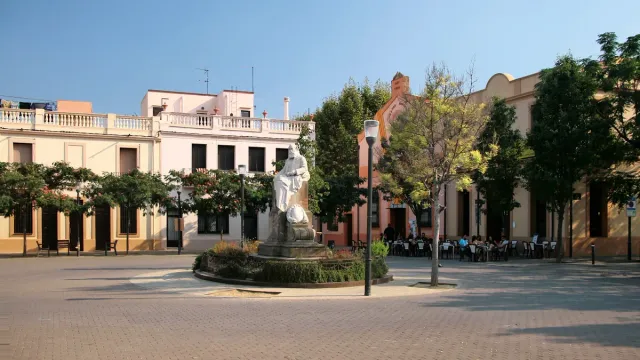 כיכר מרוצפת לבנים עם פסל לבן במרכזה ובתים נמוכים בגווני פסטל