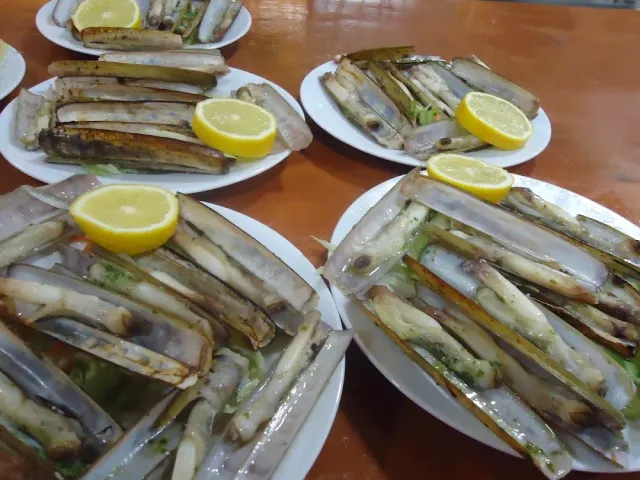 ארבע צלחות עם צדפות סכין צלויות ופלחי לימון, על שולחן עץ