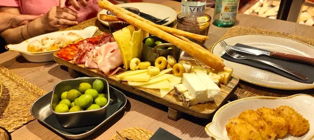 קרש עץ עם גבינות, נקניקים וזיתים, ולצדו קערת זיתים ירוקים