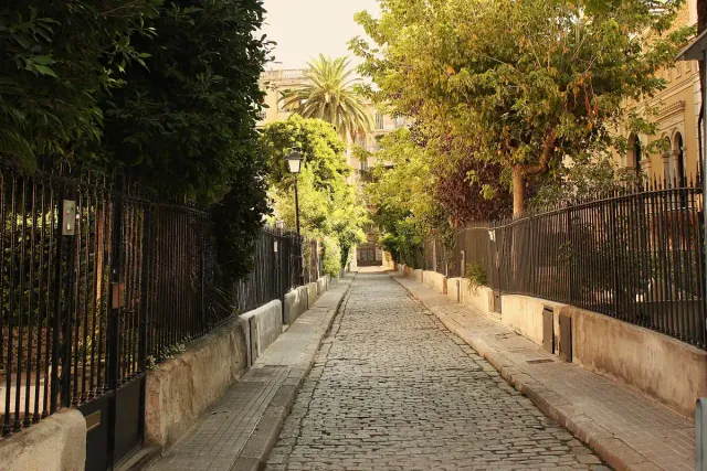 סמטה מרוצפת שקטה בין מעקות ברזל וצמחייה
