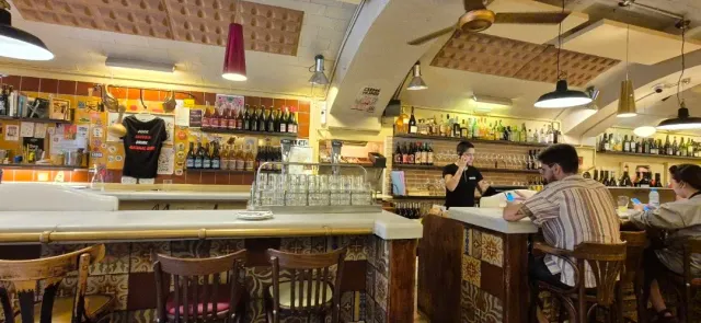 דלפק משקאות עם מדפי בקבוקים, כוסות הפוכות ויושבים על שרפרפים