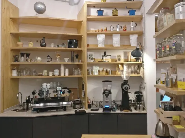 עמדת קפה עם מכונת אספרסו, מטחנה ומדפי עץ עמוסים כוסות וצנצנות
