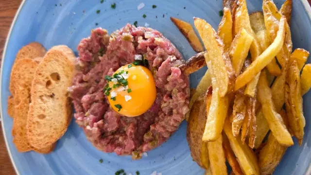 בשר טחון נא עם חלמון ביצה במרכז, תפוחי אדמה מטוגנים ולחם קלוי