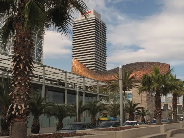 פסל דג ענק מרשת מתכת מוזהבת לצד מגדל גבוה ודקלים