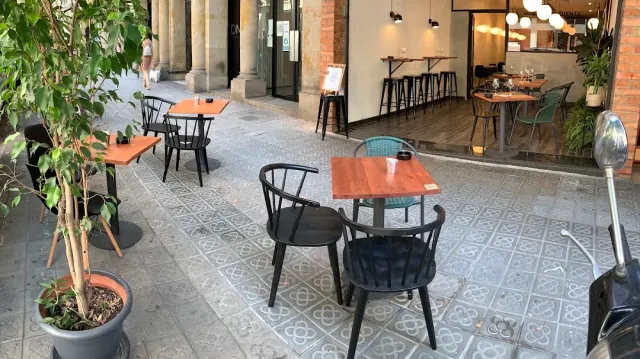 שולחנות כתומים וכיסאות שחורים על ריצוף מצויר, מתחת לקשתות מעבר
