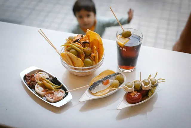 ארבע מנות קטנות עם זיתים ודגים משומרים, לצד כוס משקה כהה