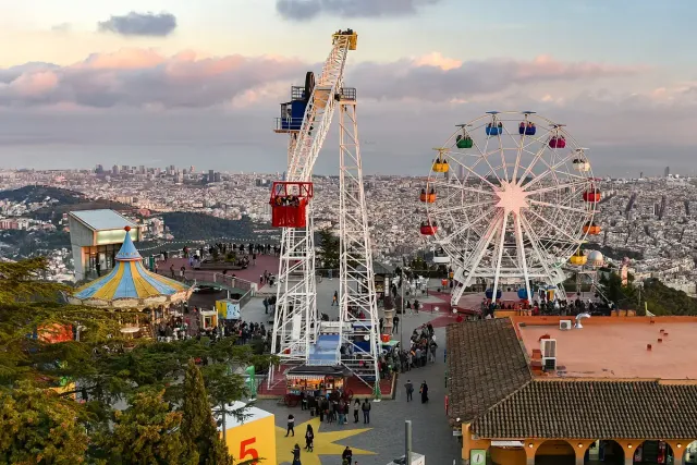 מתקני שעשועים וגלגל ענק על ראש הר ומתחתיהם העיר והים