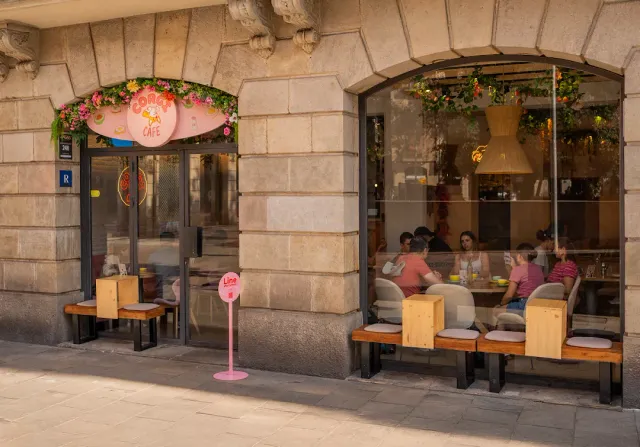 חזית אבן עם שלט מעוטר פרחים, ספסלי עץ ויושבים מאחורי חלון גדול